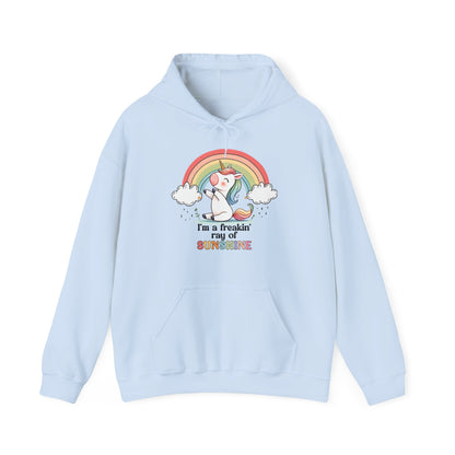 Front view of a light blue hoodie featuring a grumpy-looking unicorn with wings under a rainbow, with the text "I'm a Freakin' Ray of Sunshine." Part of the Vivid Divergence Sensory Friendly Unisex Hoodie Range.