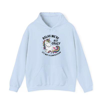 Front view of a light blue hoodie featuring the text "Relax, We're All Crazy" and a cartoon illustration of a raccoon in a teacup. Part of the Vivid Divergence Sensory Friendly Unisex Hoodie Range.