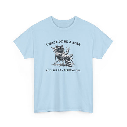 Hanging front view of a light blue T-shirt featuring a cute raccoon holding a star with text that reads "I May Not Be A Star, But I Sure Am Burning Out." Part of the Vivid Divergence Sensory Friendly Unisex Tees Range.