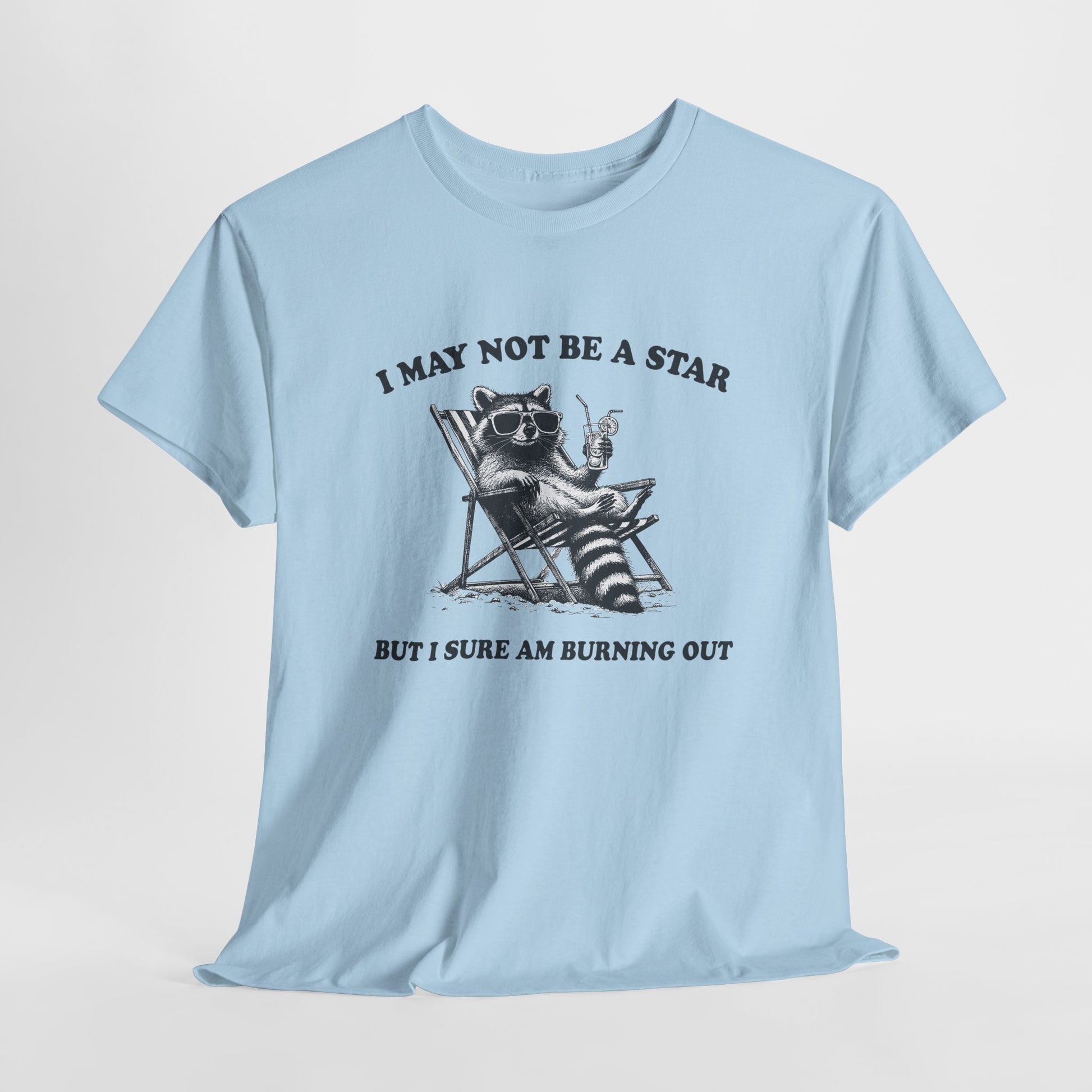 Hanging front view of a light blue T-shirt featuring a cute raccoon holding a star with text that reads "I May Not Be A Star, But I Sure Am Burning Out." Part of the Vivid Divergence Sensory Friendly Unisex Tees Range.