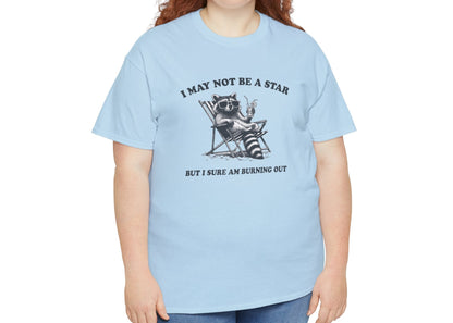 Modeled front view of a light blue T-shirt featuring a cute raccoon holding a star with text that reads "I May Not Be A Star, But I Sure Am Burning Out." Part of the Vivid Divergence Sensory Friendly Unisex Tees Range.