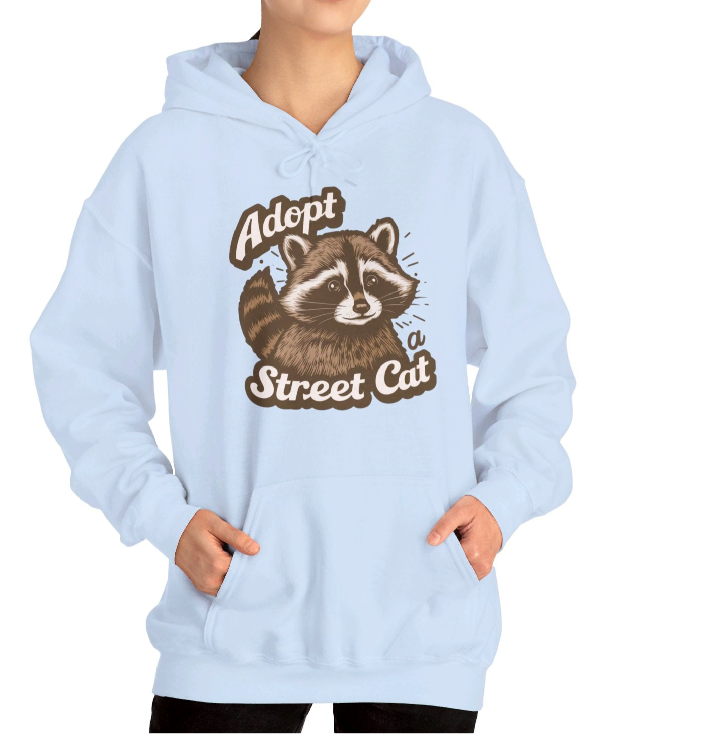 Model wearing a light blue hoodie with the text "Adopt a Street Cat" and a cartoon illustration of a raccoon holding a cup. Part of the Vivid Divergence Sensory Friendly Unisex Hoodie Range.