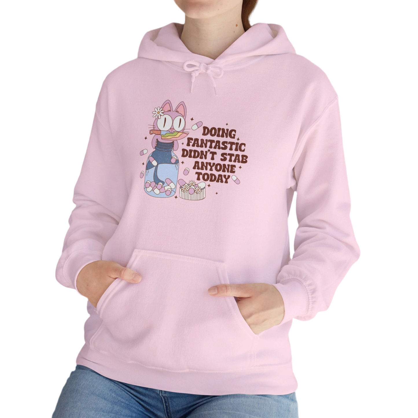 Model wearing a light pink hoodie featuring the text "Doing Fantastic, Didn’t Stab Anyone Today" and a cartoon illustration of a raccoon holding a knife. Part of the Vivid Divergence Sensory Friendly Unisex Hoodie Range.