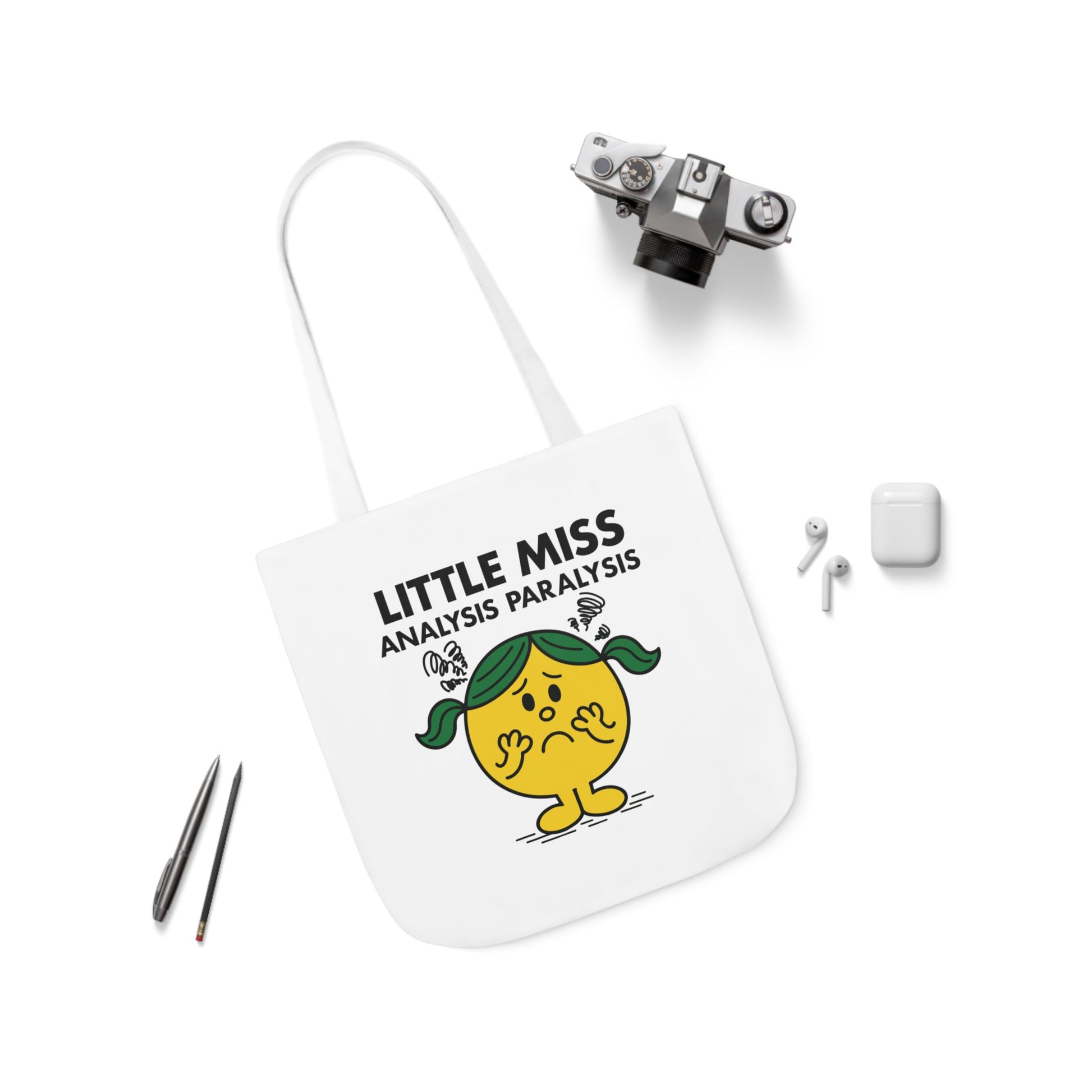 Flat lay of tote bag featuring Little Miss Analysis Paralysis surrounded by scattered accessories. Should she organize her thoughts or her pens first? Part of the Vivid Divergence Little Miss Meme Collection!

