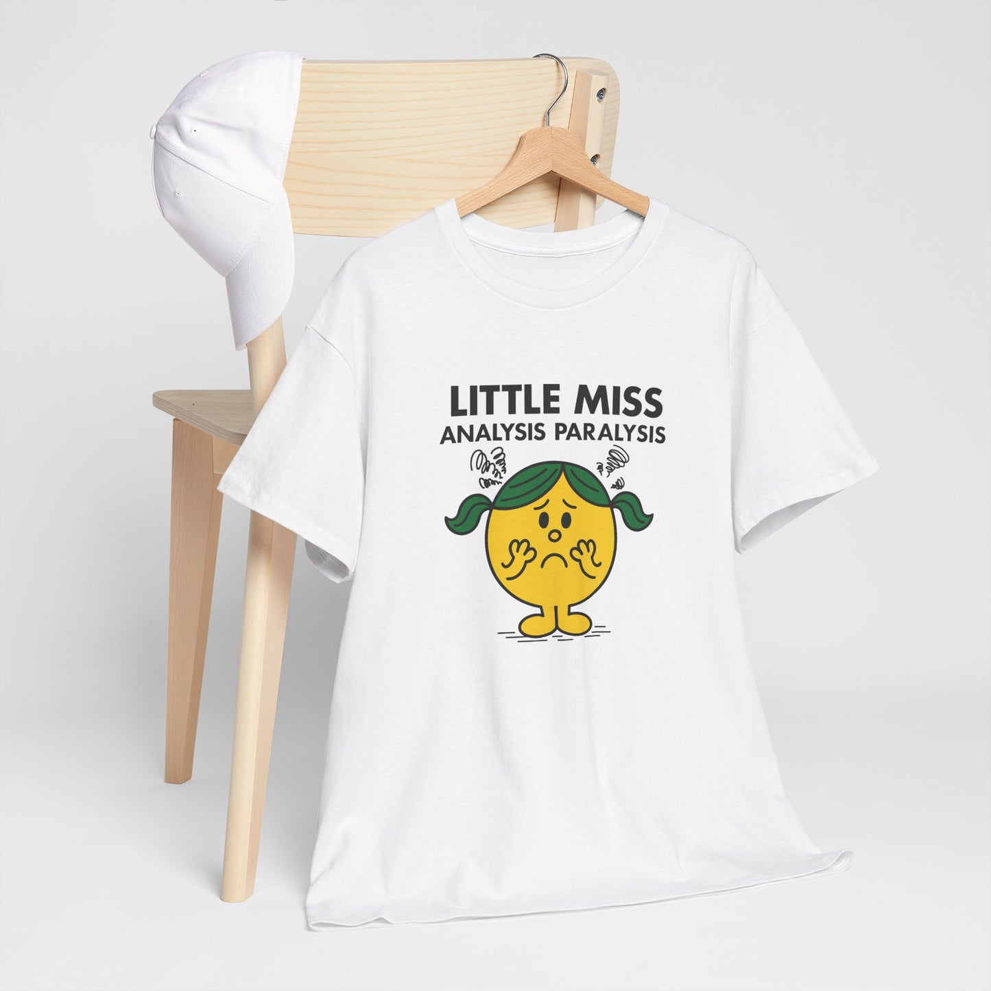 Little Miss Analysis Paralysis T-shirt draped over a wooden chair in a lifestyle setting. Part of the Little Miss Meme Character Collection. A Vivid Divergence Sensory Friendly Unisex Tee.
