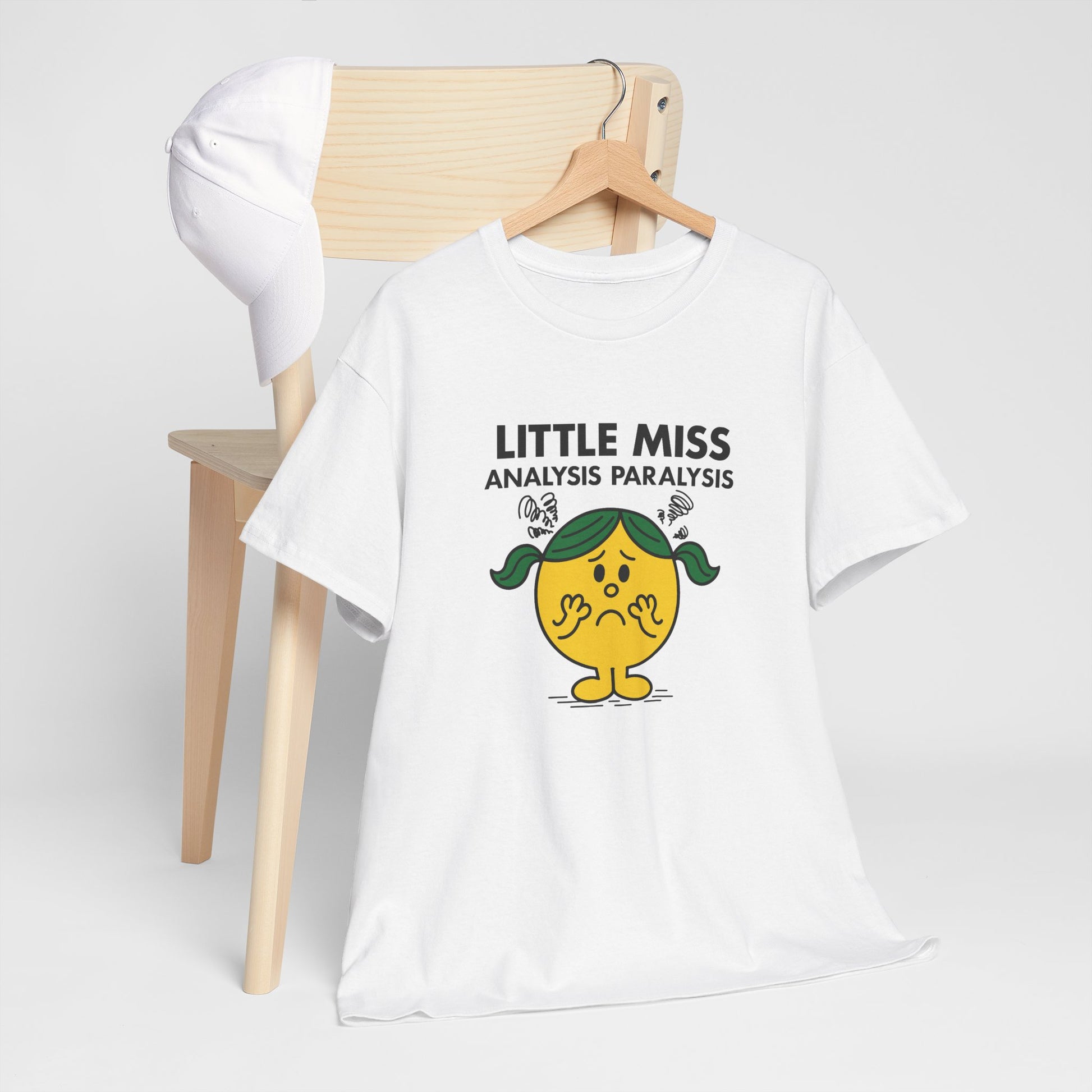 Little Miss Analysis Paralysis T-shirt draped over a wooden chair in a lifestyle setting. Part of the Little Miss Meme Character Collection. A Vivid Divergence Sensory Friendly Unisex Tee.
