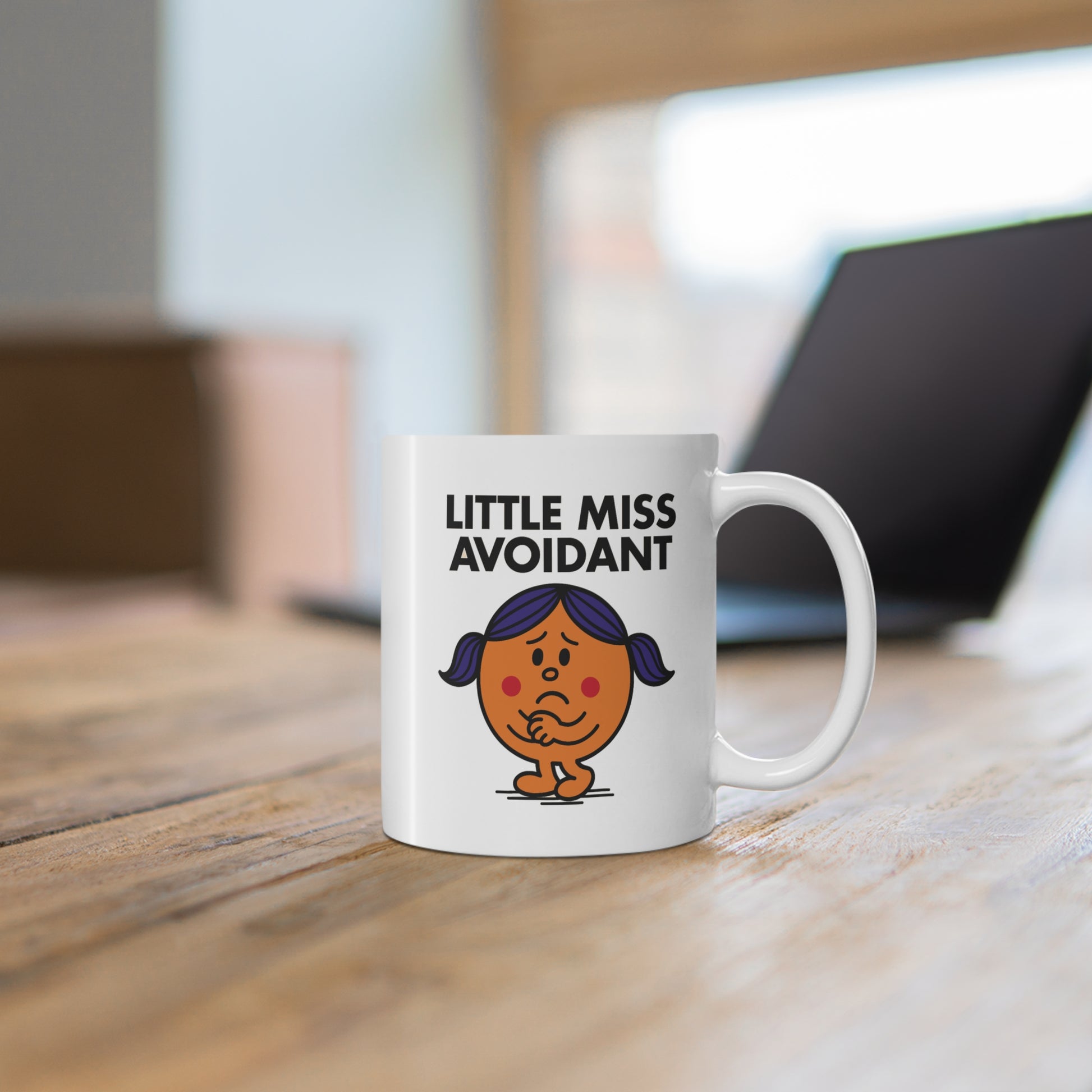 White mug on wooden table beside a laptop. Design features Little Miss Avoidant nervously preparing to ghost your last message. Part of the Vivid Divergence Little Miss Meme Collection!
