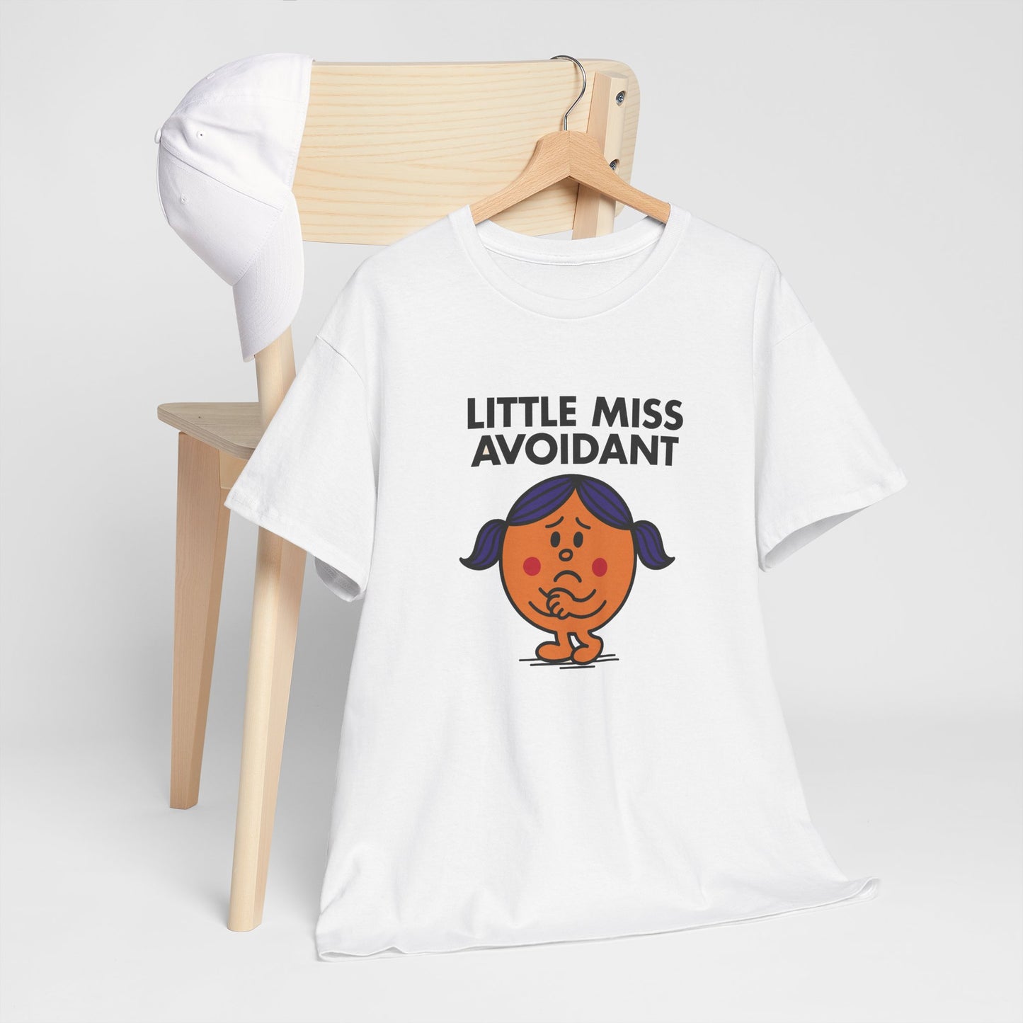 Little Miss Avoidant T-shirt draped over a wooden chair in a relaxed setting. Part of the Little Miss Meme Character Collection. A Vivid Divergence Sensory Friendly Unisex Tee.