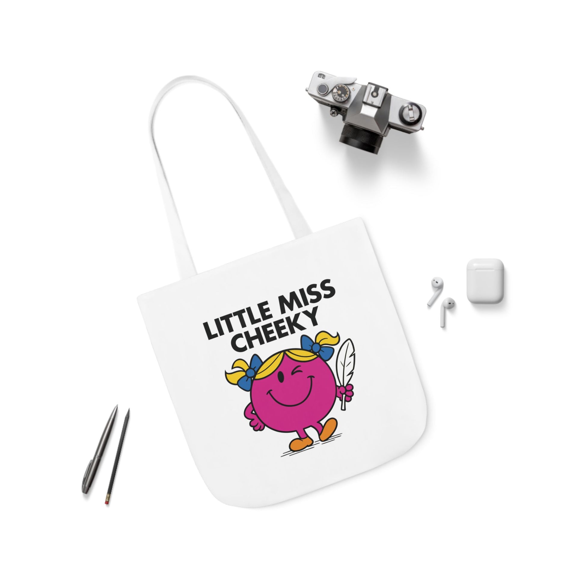 Flat lay of tote bag featuring Little Miss Cheeky surrounded by pens and earbuds — tools for doodling and dodging drama. Part of the Vivid Divergence Little Miss Meme Collection!
