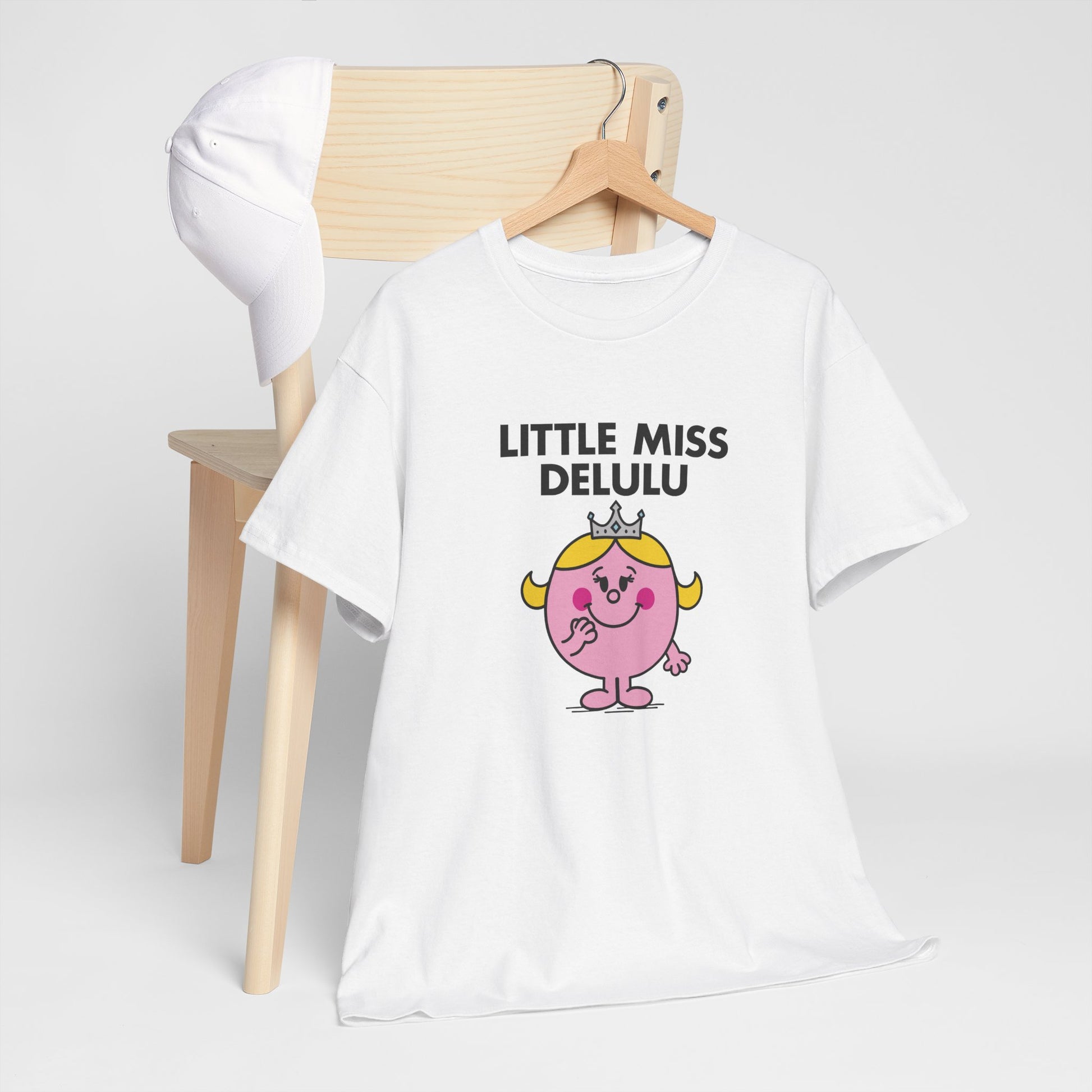 Little Miss Delulu T-shirt draped over a wooden chair in a minimal setting. Part of the Little Miss Meme Character Collection. A Vivid Divergence Sensory Friendly Unisex Tee.
