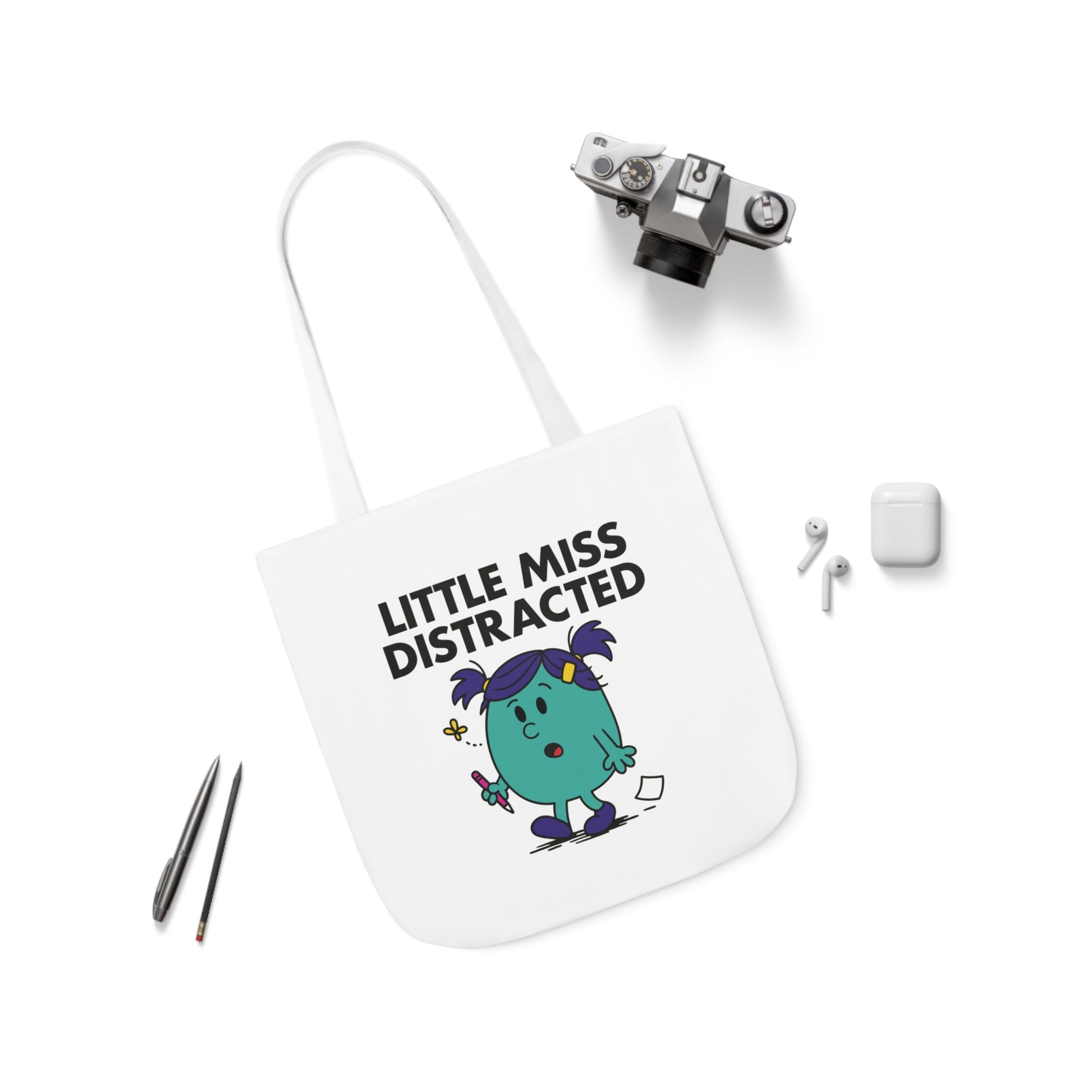 Flat lay of tote bag featuring Little Miss Distracted surrounded by accessories. She opened the tote to clean it, now she’s deep in a horoscope rabbit hole. Part of the Vivid Divergence Little Miss Meme Collection!
