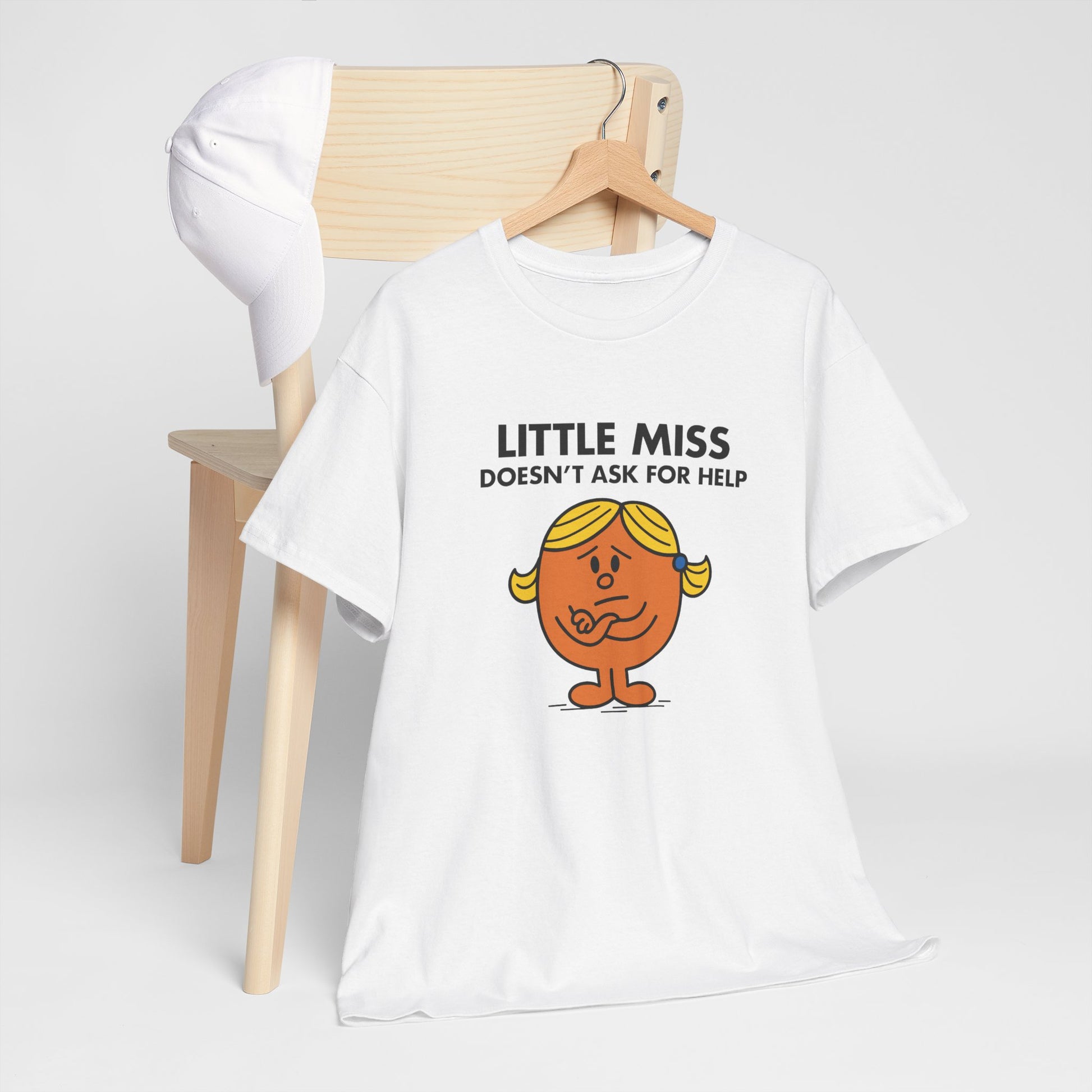 Little Miss Doesn’t Ask For Help T-shirt draped over a wooden chair in a light setting. Part of the Little Miss Meme Character Collection. A Vivid Divergence Sensory Friendly Unisex Tee.
