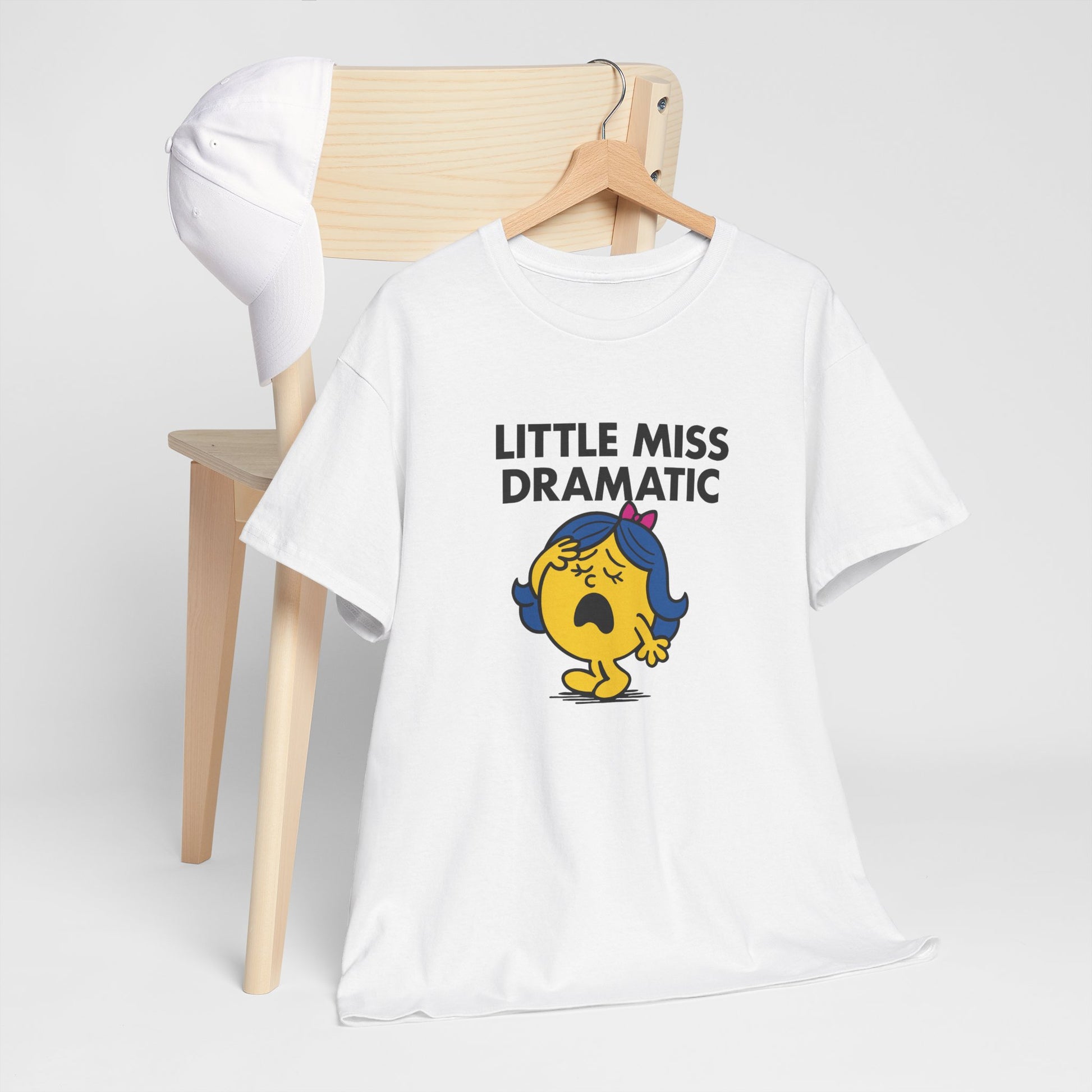 Little Miss Dramatic T-shirt draped over a wooden chair in a clean setup. Part of the Little Miss Meme Character Collection. A Vivid Divergence Sensory Friendly Unisex Tee.
