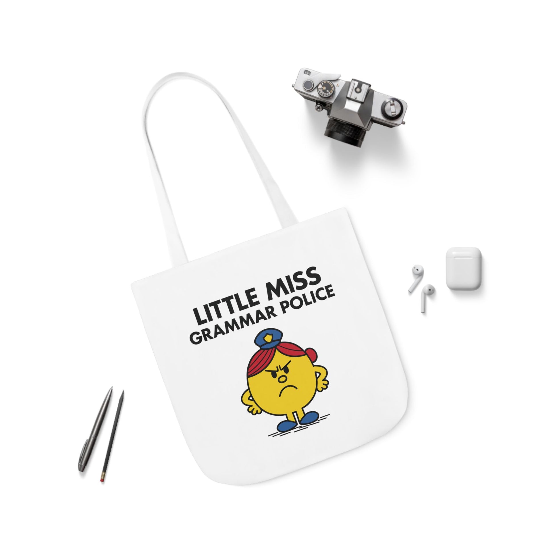 Flat lay of tote bag featuring Little Miss Grammar Police surrounded by pens and accessories. She brought a red pen to brunch. Part of the Vivid Divergence Little Miss Meme Collection!
