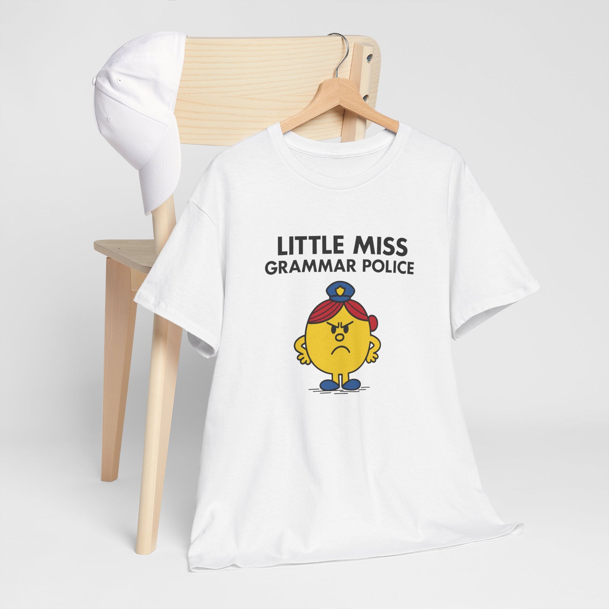 Little Miss Grammar Police T-shirt draped over a wooden chair in a minimalist space. Part of the Little Miss Meme Character Collection. A Vivid Divergence Sensory Friendly Unisex Tee.
