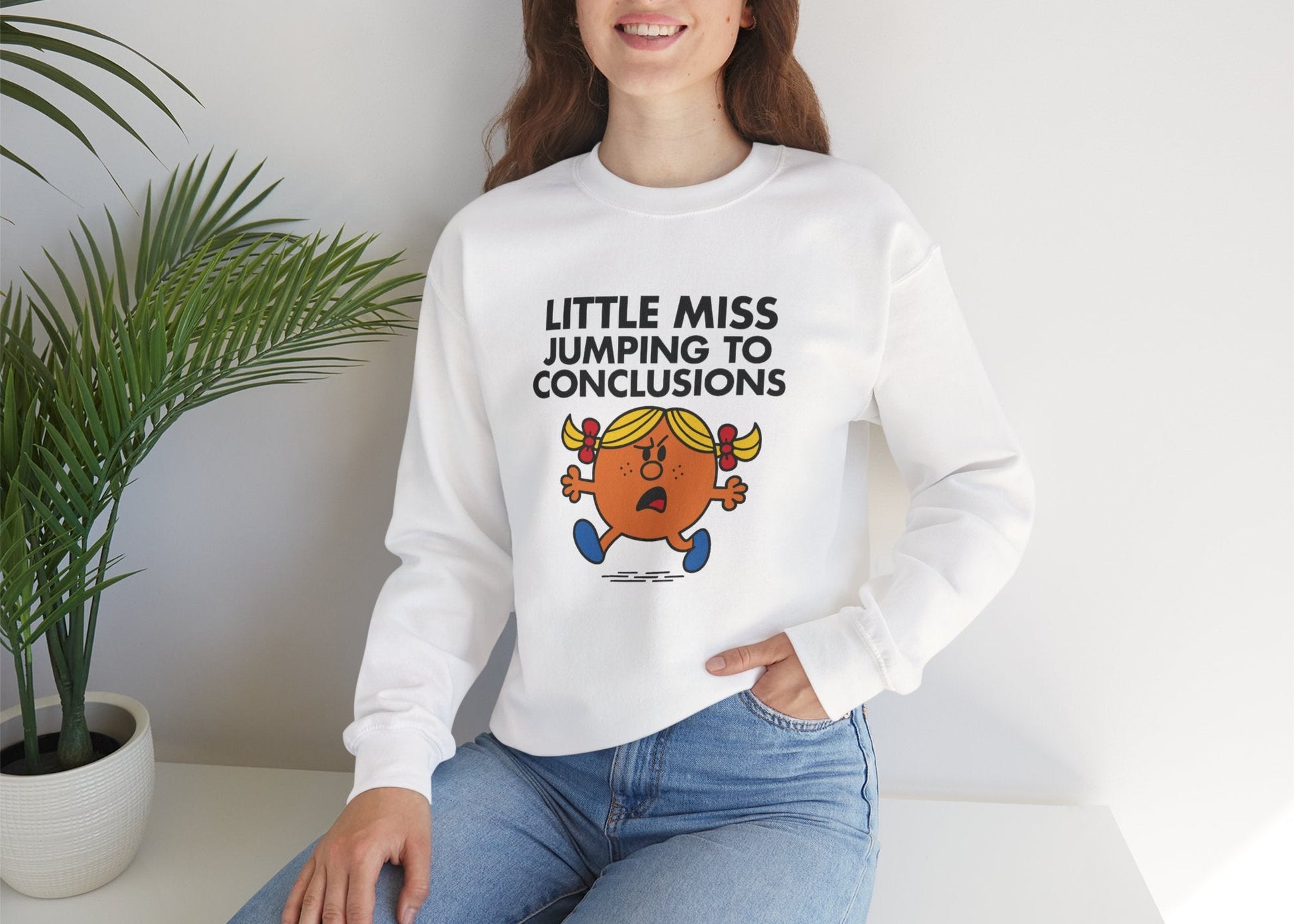 Person wearing the Little Miss Jumping To Conclusions sweatshirt while seated. Part of the Little Miss Meme Character Collection. A Vivid Divergence Sensory Friendly Sweater Jumper.
