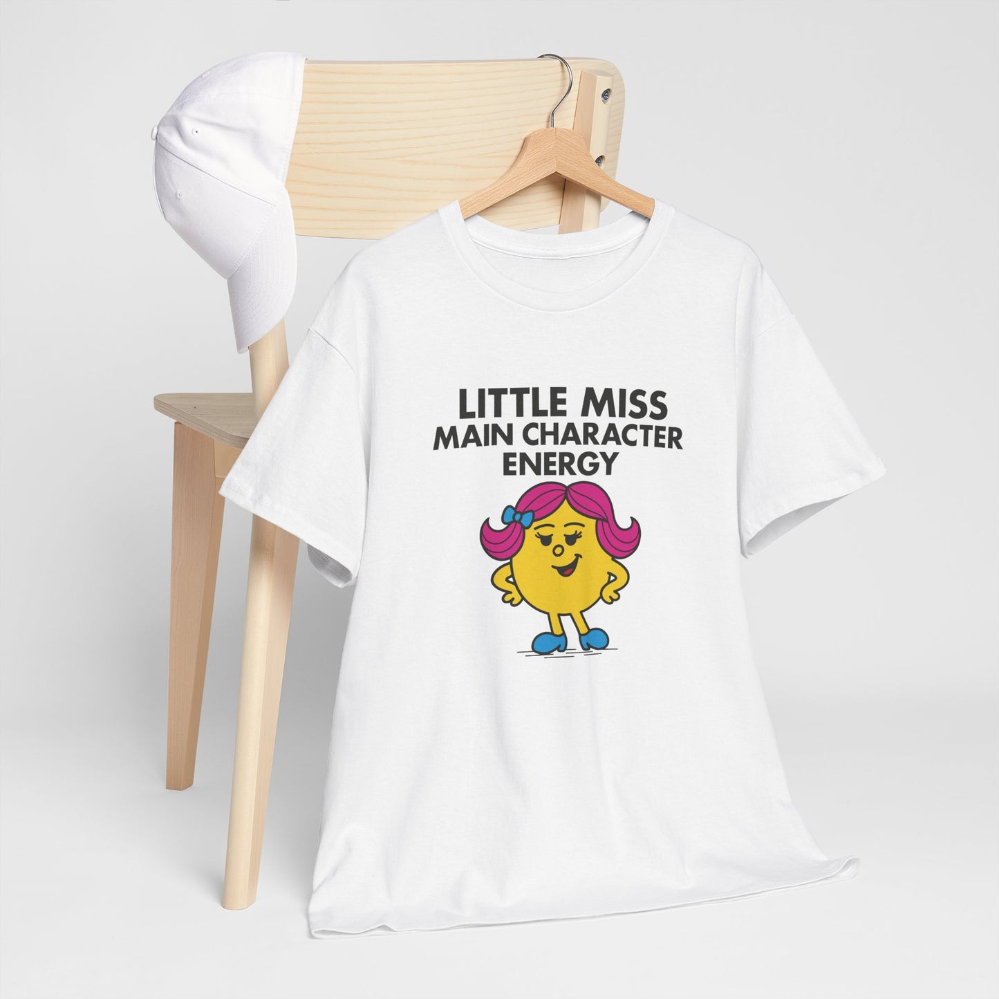 Little Miss Main Character Energy T-shirt draped over a wooden chair in a minimalist setting. Part of the Little Miss Meme Character Collection. A Vivid Divergence Sensory Friendly Unisex Tee.
