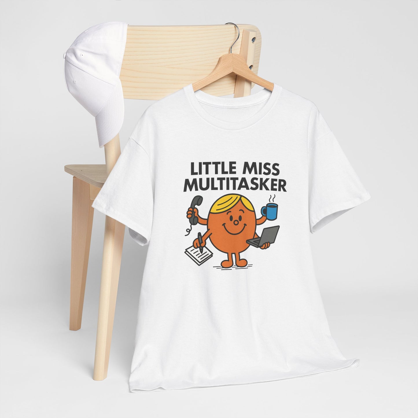 Little Miss Multitasker T-shirt draped over a wooden chair in a casual setup. Part of the Little Miss Meme Character Collection. A Vivid Divergence Sensory Friendly Unisex Tee.
