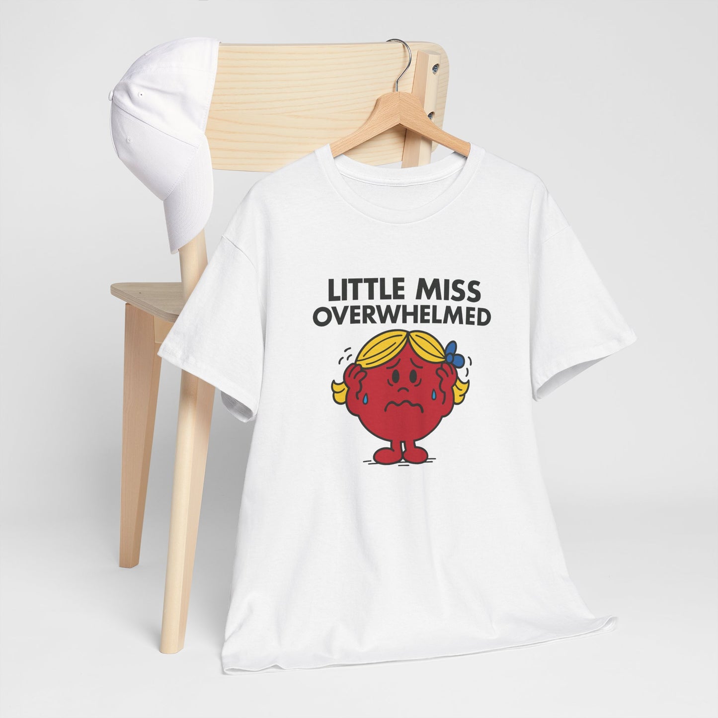 Little Miss Overwhelmed T-shirt draped over a wooden chair in a cozy setup. Part of the Little Miss Meme Character Collection. A Vivid Divergence Sensory Friendly Unisex Tee.
