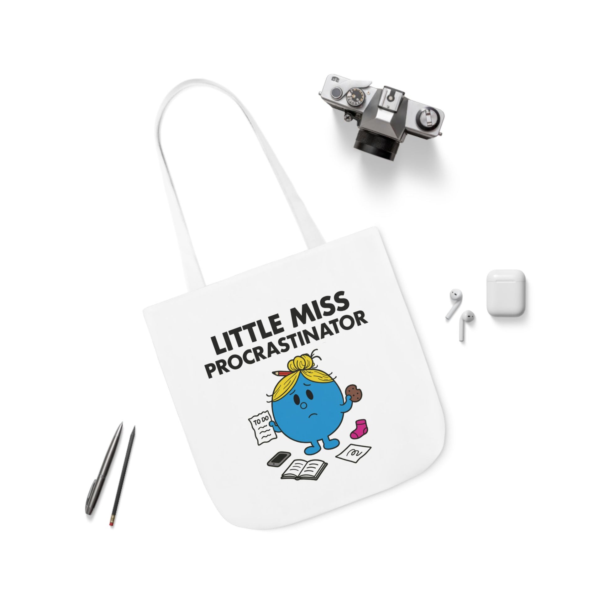 Flat lay of tote bag featuring Little Miss Procrastinator surrounded by earbuds and pens — aka tools she hasn’t touched all day. Part of the Vivid Divergence Little Miss Meme Collection!
