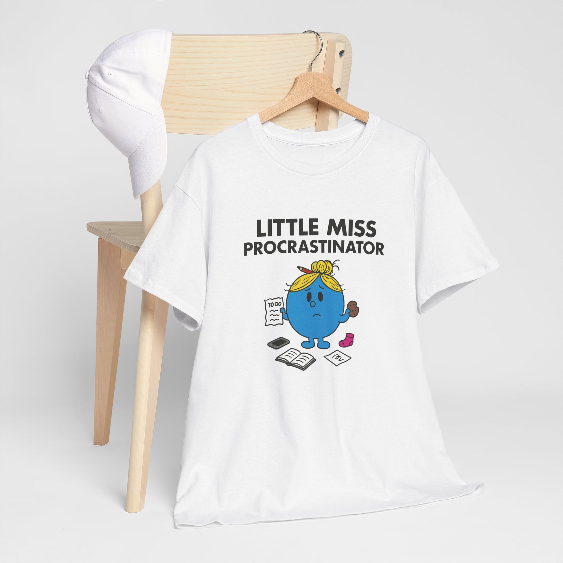 Little Miss Procrastinator T-shirt draped over a wooden chair in a simple setup. Part of the Little Miss Meme Character Collection. A Vivid Divergence Sensory Friendly Unisex Tee.

