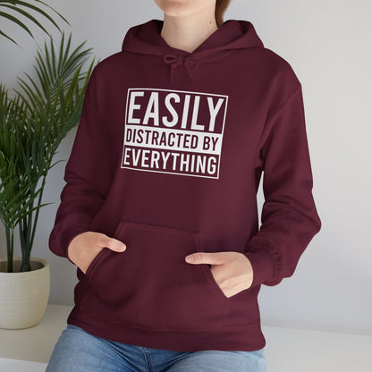 Model wearing a maroon hoodie with the text "Easily Distracted by Everything" in bold white lettering. Part of the Vivid Divergence Sensory Friendly Unisex Hoodie Range.