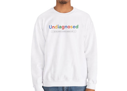 Model wearing a white sweatshirt with "Undiagnosed" in a Google-style font and a search bar graphic, standing with a neutral expression. Part of the Vivid Divergence Sensory Friendly Unisex Sweater Jumper Range.