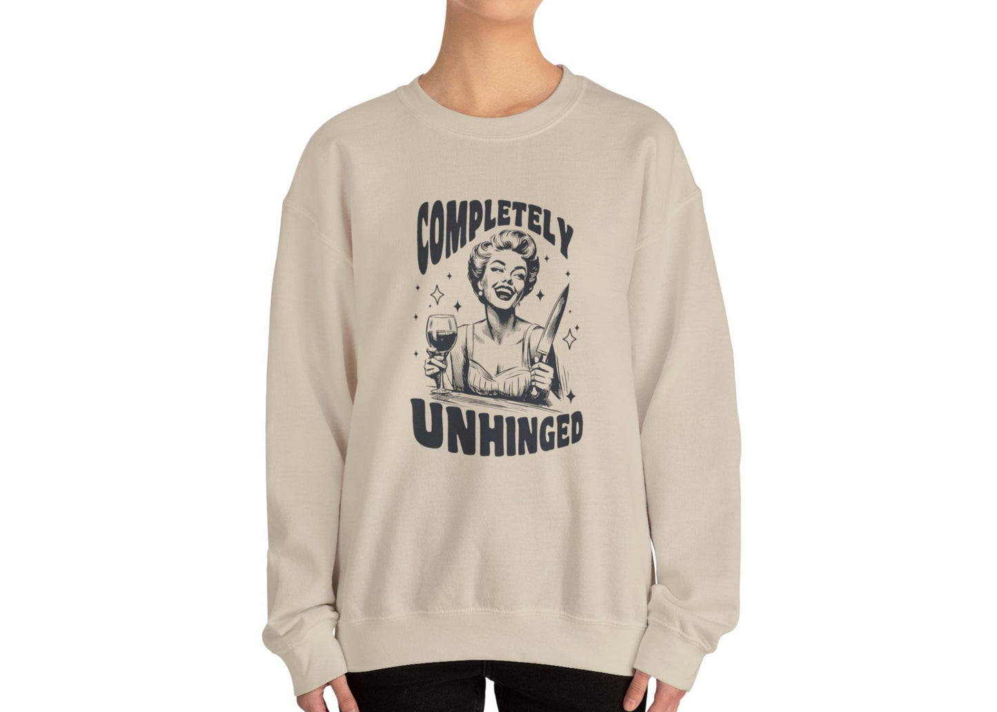 Model wearing a beige sweatshirt with a graphic of a woman holding a knife and a glass of wine and the text "Completely Unhinged," standing with hands at sides. Part of the Vivid Divergence Sensory Friendly Unisex Sweater Jumper Range.