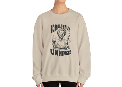 Model wearing a beige sweatshirt with a graphic of a woman holding a knife and a glass of wine and the text "Completely Unhinged," standing with hands at sides. Part of the Vivid Divergence Sensory Friendly Unisex Sweater Jumper Range.
