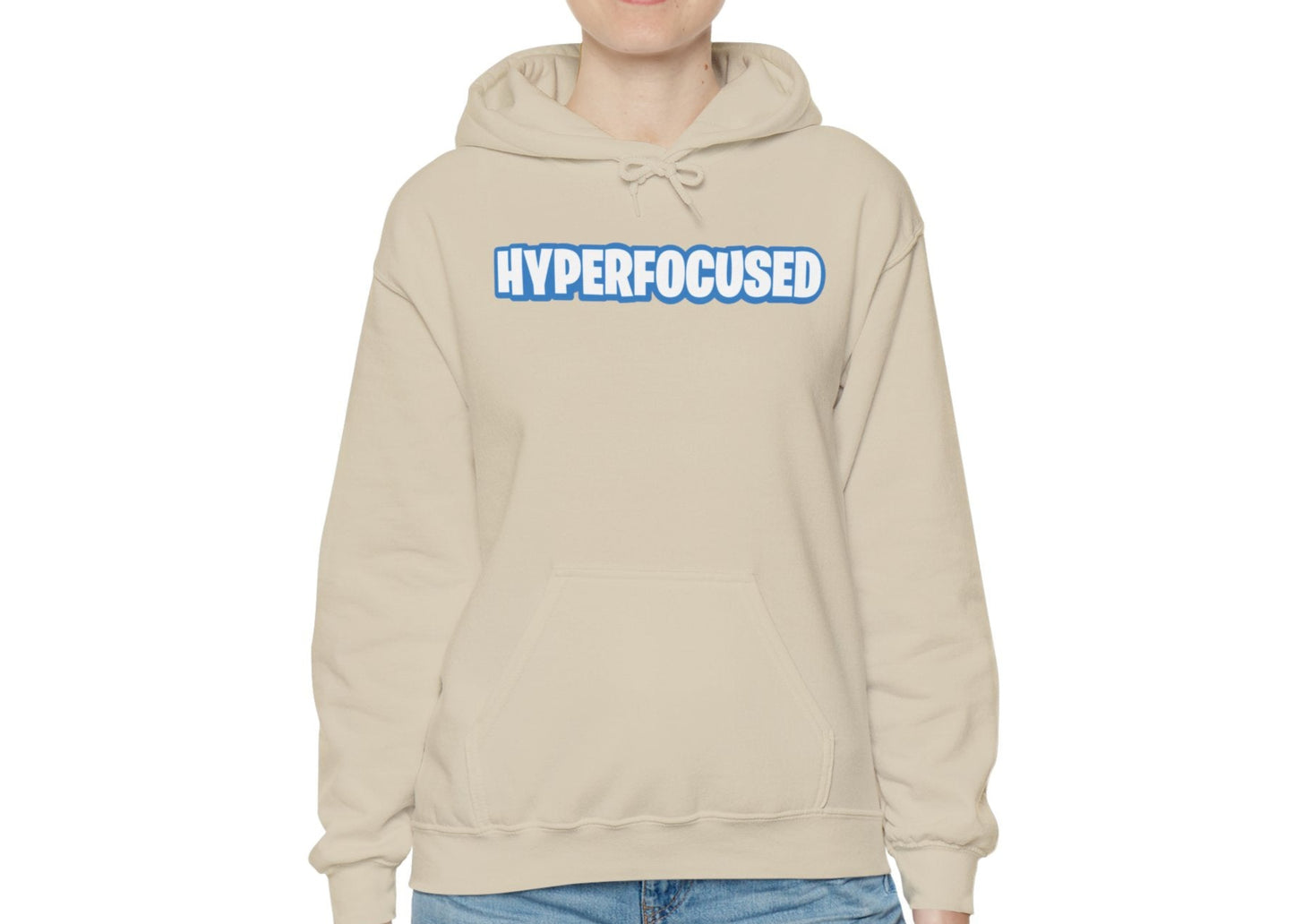 Model wearing a beige hoodie with the word "HYPERFOCUSED" in a bold, blue Fortnite-style font, standing with hands at sides. Part of the Vivid Divergence Sensory Friendly Unisex Hoodie Range.