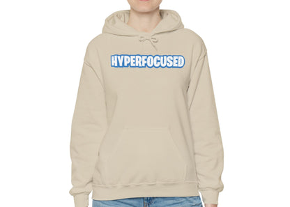 Model wearing a beige hoodie with the word "HYPERFOCUSED" in a bold, blue Fortnite-style font, standing with hands at sides. Part of the Vivid Divergence Sensory Friendly Unisex Hoodie Range.