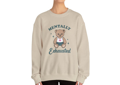 Model wearing a beige sweatshirt with a cute teddy bear wearing an apron and the text "Mentally Exhausted," standing with hands at sides. Part of the Vivid Divergence Sensory Friendly Unisex Sweater Jumper Range.