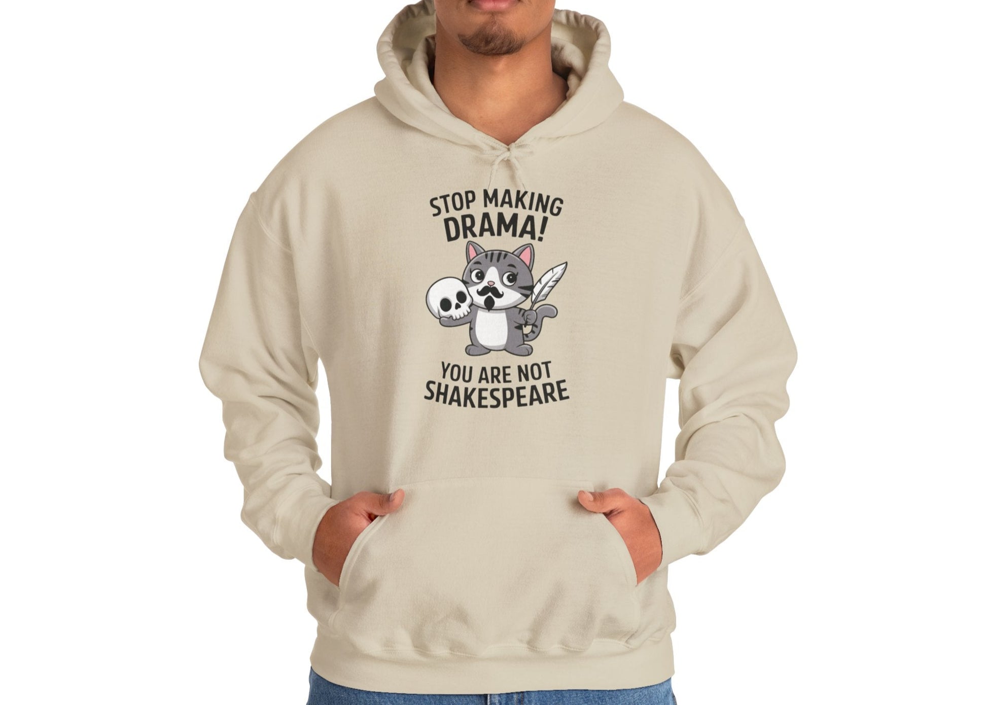 Model wearing a beige hoodie with a cartoon cat holding a skull and the text "Stop Making Drama! You Are Not Shakespeare," standing with hands in pockets. Part of the Vivid Divergence Sensory Friendly Unisex Hoodie Range.