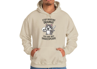 Model wearing a beige hoodie with a cartoon cat holding a skull and the text "Stop Making Drama! You Are Not Shakespeare," standing with hands in pockets. Part of the Vivid Divergence Sensory Friendly Unisex Hoodie Range.