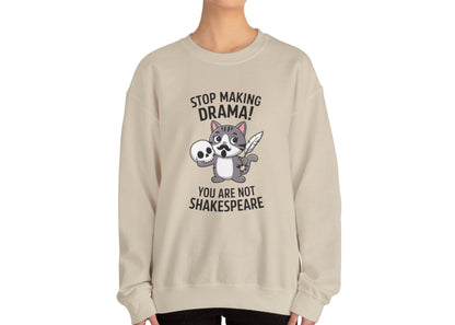Model wearing a beige sweatshirt with a cartoon cat holding a skull and the text "Stop Making Drama! You Are Not Shakespeare," standing with hands at sides. Part of the Vivid Divergence Sensory Friendly Unisex Sweater Jumper Range.