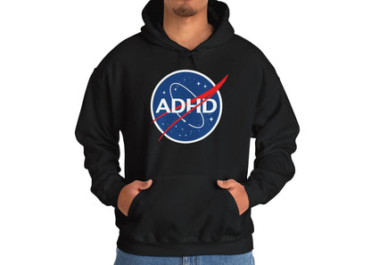 Model wearing a black hoodie with a NASA-inspired logo and the word "ADHD," standing with hands in pockets. Part of the Vivid Divergence Sensory Friendly Unisex Hoodie Range.