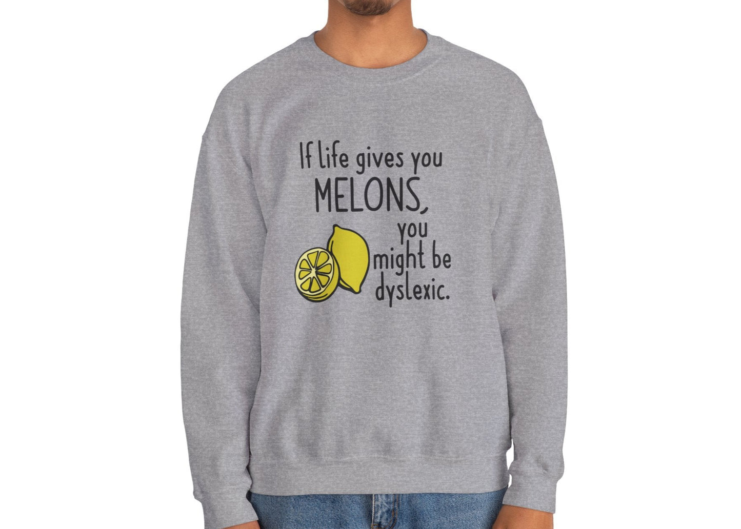 Model wearing a gray sweatshirt with an illustration of melons and the text "If Life Gives You Melons, You Might Be Dyslexic," standing with hands at sides. Part of the Vivid Divergence Sensory Friendly Unisex Sweater Jumper Range.