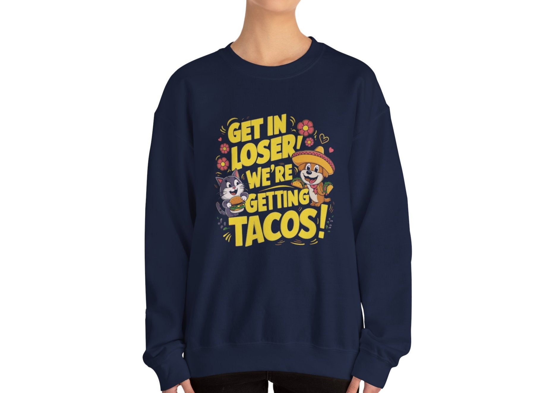 Model wearing a navy blue sweatshirt with colorful cartoon animals and the text "Get in Loser, We're Getting Tacos!" standing with hands at sides. Part of the Vivid Divergence Sensory Friendly Unisex Sweater Jumper Range.