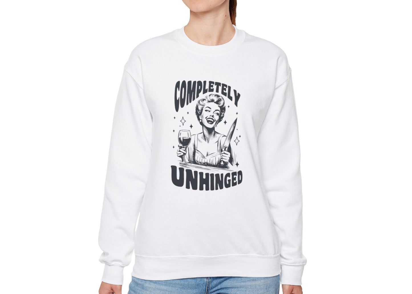 Model wearing a white sweatshirt with a graphic of a woman holding a knife and a glass of wine and the text "Completely Unhinged," standing with hands at sides. Part of the Vivid Divergence Sensory Friendly Unisex Sweater Jumper Range.