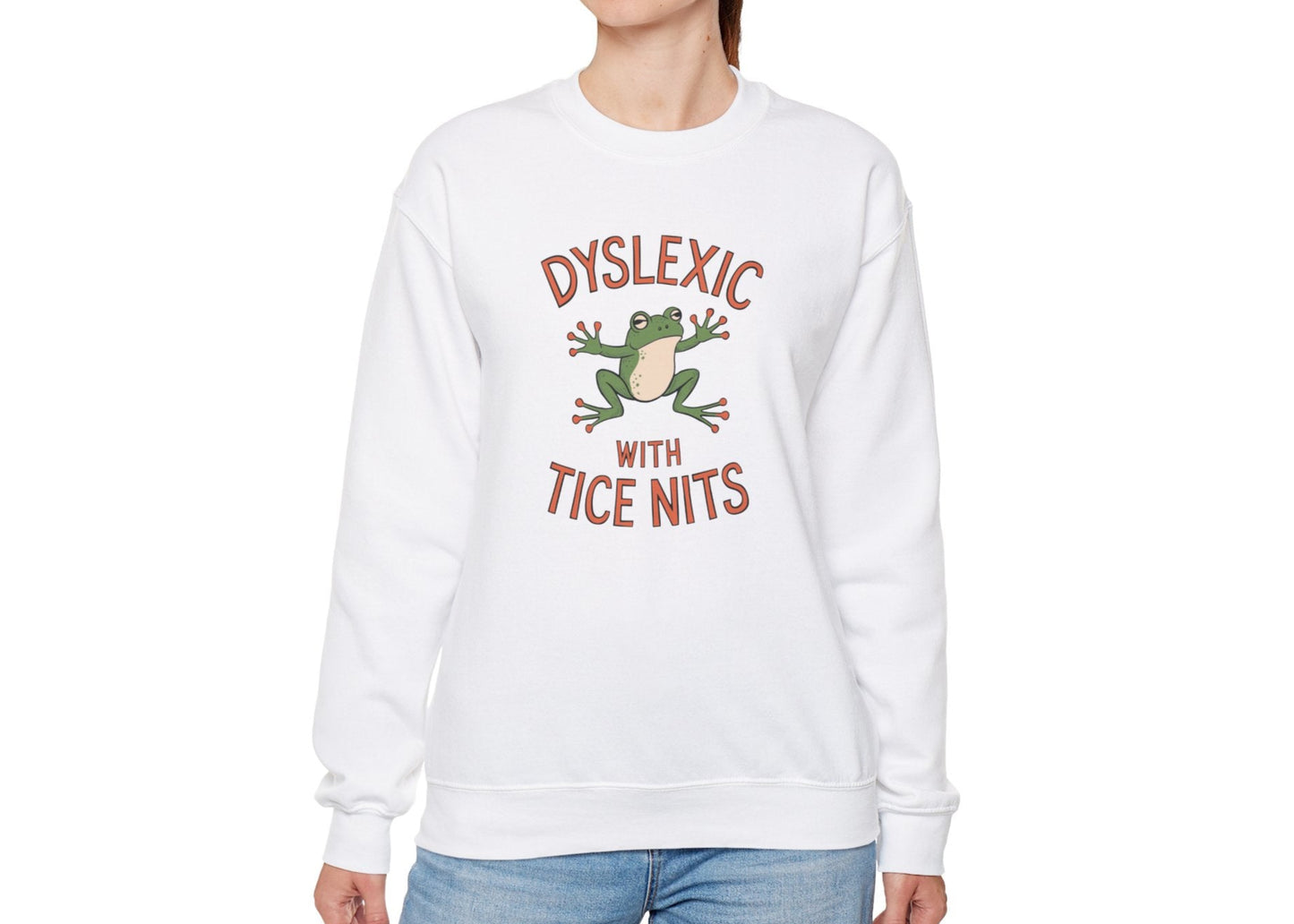 Model wearing a white sweatshirt with a cartoon frog and the text "Dyslexic with Tice Nits," standing with hands at sides. Part of the Vivid Divergence Sensory Friendly Unisex Sweater Jumper Range.