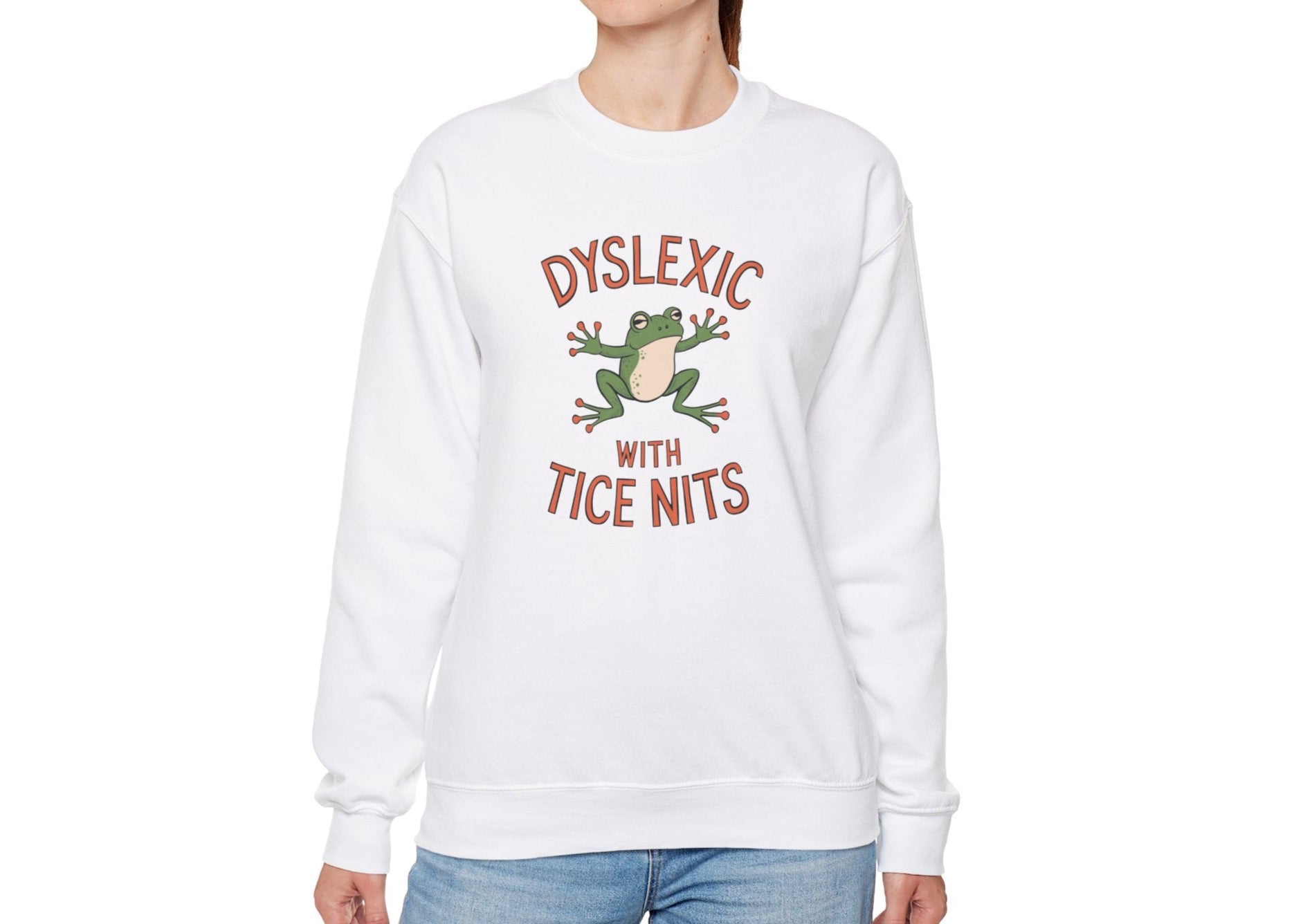 Model wearing a white sweatshirt with a cartoon frog and the text "Dyslexic with Tice Nits," standing with hands at sides. Part of the Vivid Divergence Sensory Friendly Unisex Sweater Jumper Range.