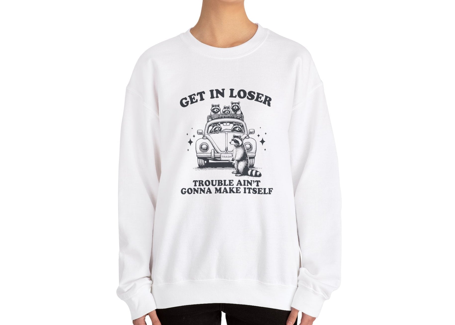 Model wearing a white sweatshirt with "Get in Loser, Trouble Ain't Gonna Cause Itself" in black letters and a group of raccoons in a car, standing with hands at sides. Part of the Vivid Divergence Sensory Friendly Unisex Sweater Jumper Range.