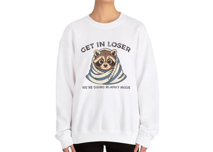 Model wearing a white sweatshirt with a raccoon wrapped in a blanket and the text "Get in Loser, We're Going Blanky Mode," standing with hands at sides. Part of the Vivid Divergence Sensory Friendly Unisex Sweater Jumper Range.