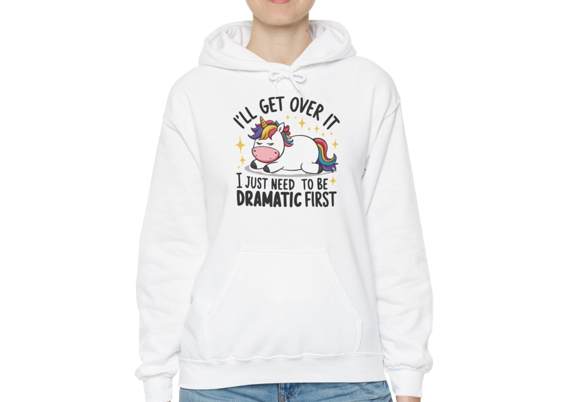 Model wearing a white hoodie with a cartoon unicorn lying dramatically on a couch and the text "I'll Get Over It, I Just Need To Be Dramatic First," standing with hands at sides. Part of the Vivid Divergence Sensory Friendly Unisex Hoodie Range.