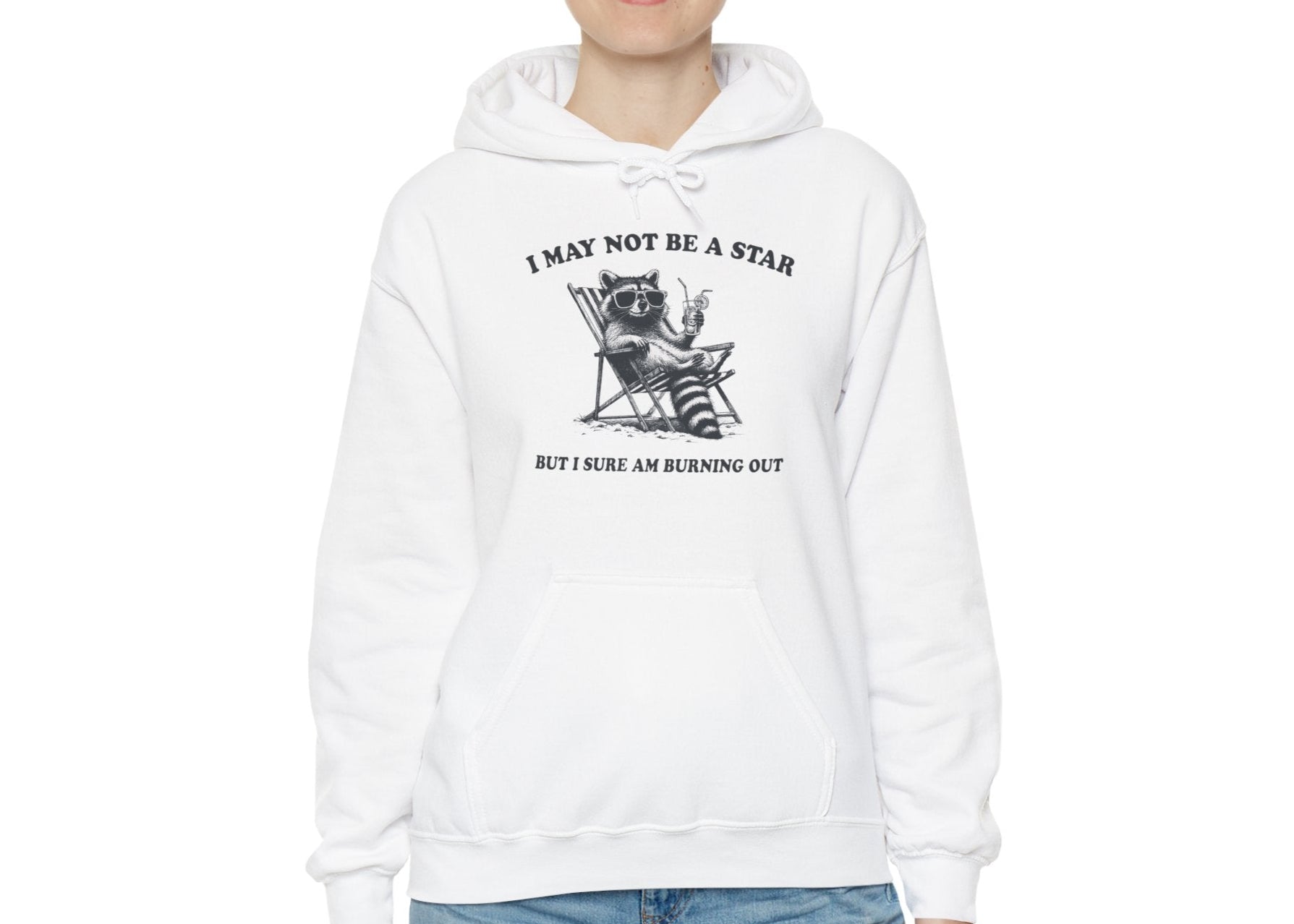 Model wearing a white hoodie with a raccoon sitting in a trash can and the text "I May Not Be A Star, But I Sure Am Burning Out," standing with hands in pockets. Part of the Vivid Divergence Sensory Friendly Unisex Hoodie Range.