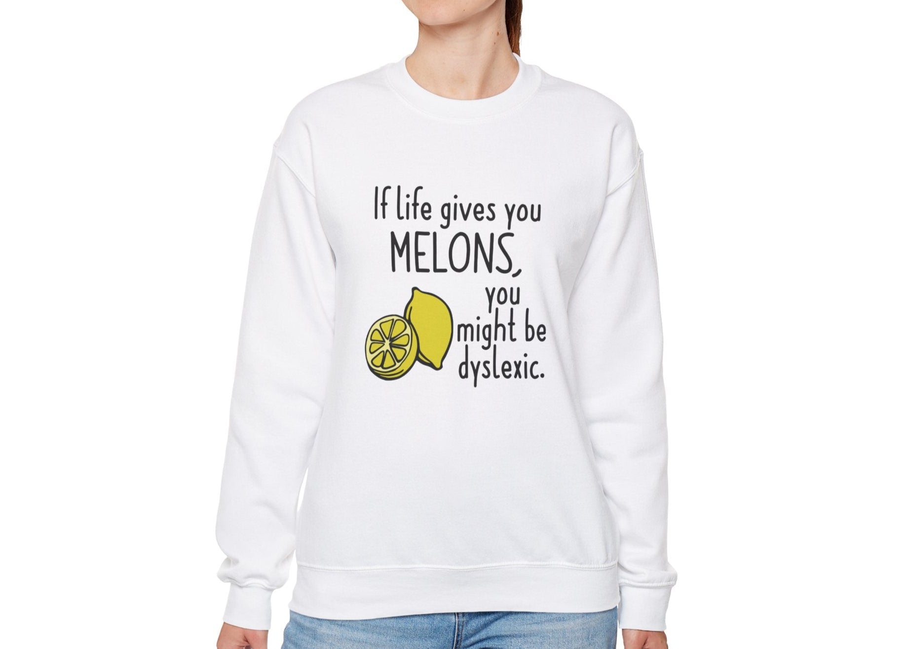 Model wearing a white sweatshirt with an illustration of melons and the text "If Life Gives You Melons, You Might Be Dyslexic," standing with hands at sides. Part of the Vivid Divergence Sensory Friendly Unisex Sweater Jumper Range.