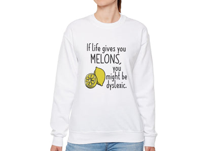 Model wearing a white sweatshirt with an illustration of melons and the text "If Life Gives You Melons, You Might Be Dyslexic," standing with hands at sides. Part of the Vivid Divergence Sensory Friendly Unisex Sweater Jumper Range.