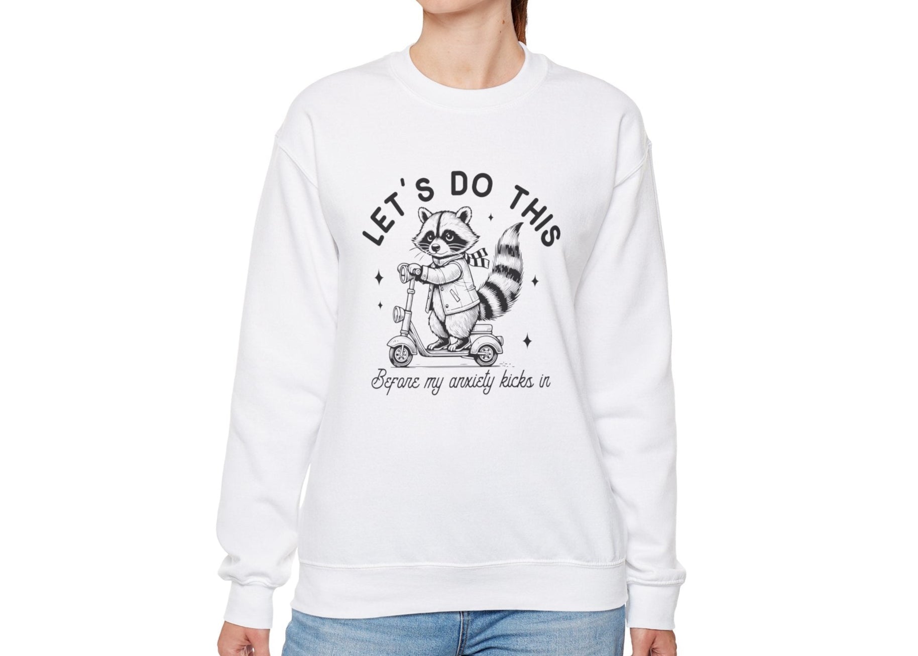 Model wearing a white sweatshirt with a cartoon raccoon riding a scooter and the text "Let's Do This Before My Anxiety Kicks In," standing with hands at sides. Part of the Vivid Divergence Sensory Friendly Unisex Sweater Jumper Range.