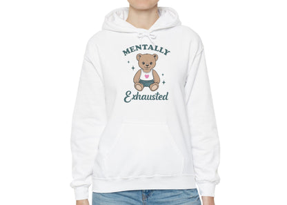 Model wearing a white hoodie with a cute teddy bear wearing an apron and the text "Mentally Exhausted," standing with hands at sides. Part of the Vivid Divergence Sensory Friendly Unisex Hoodie Range. 