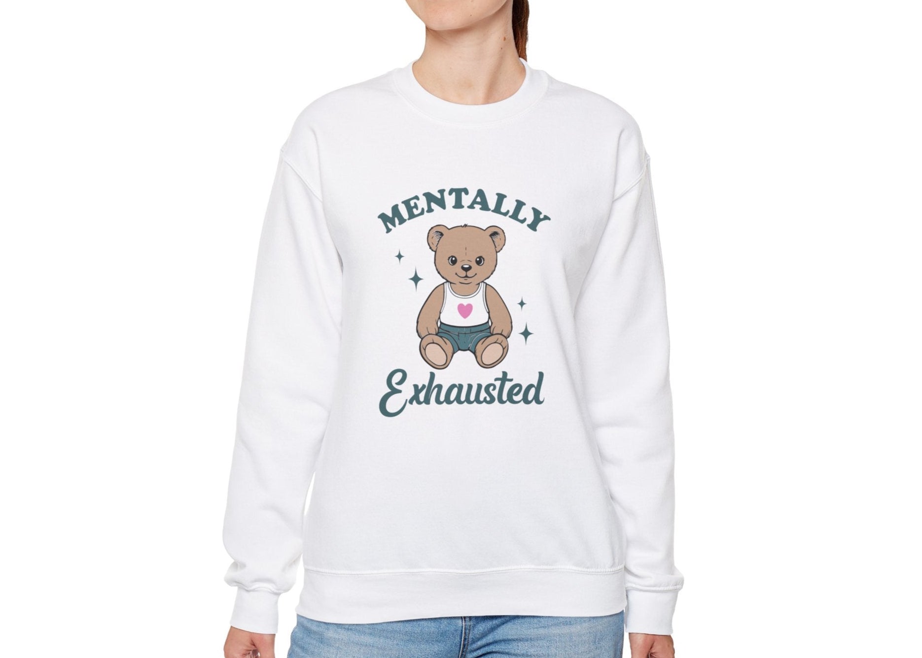 Model wearing a white sweatshirt with a cute teddy bear wearing an apron and the text "Mentally Exhausted," standing with hands at sides. Part of the Vivid Divergence Sensory Friendly Unisex Sweater Jumper Range.